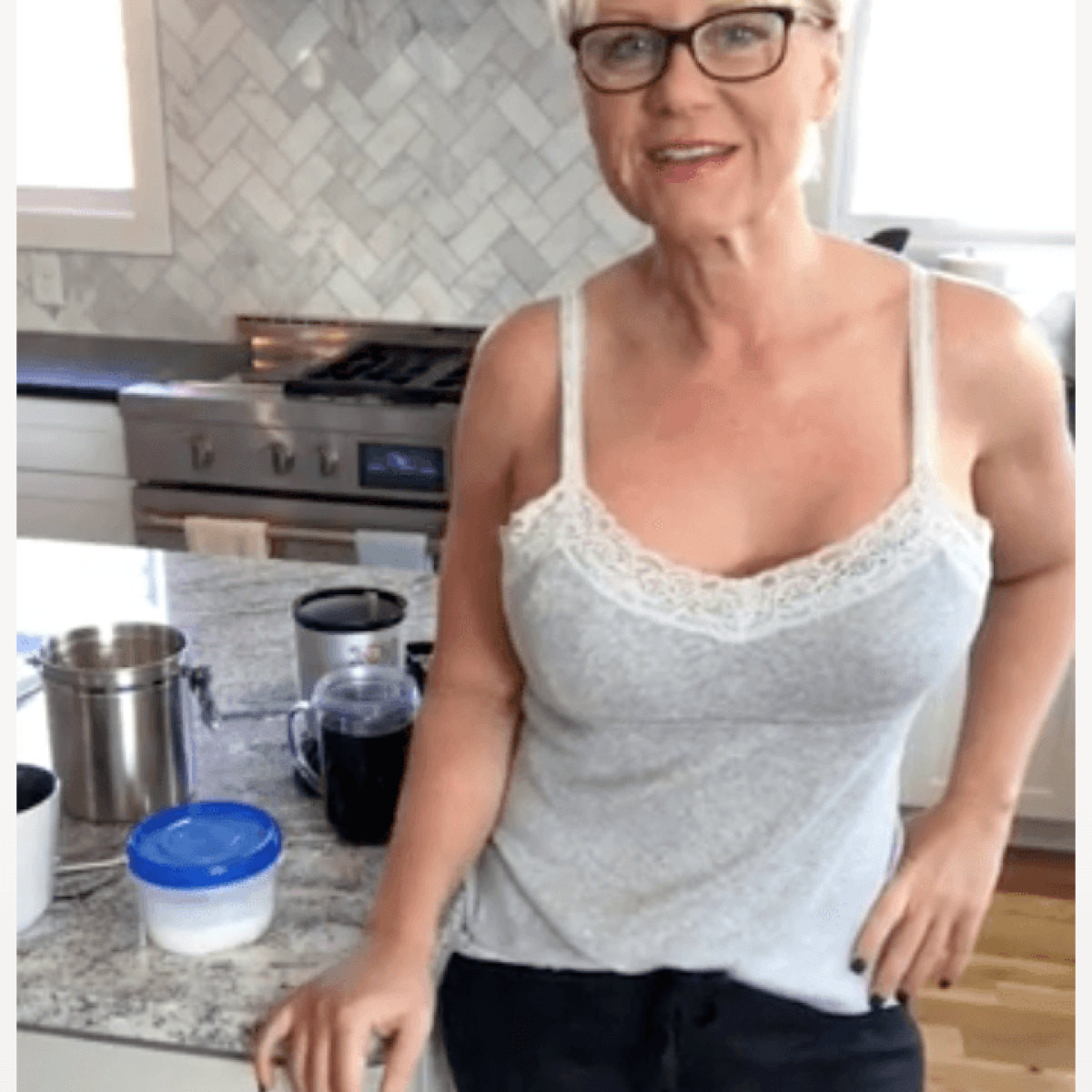 A woman in glasses standing in front of a kitchen counter.